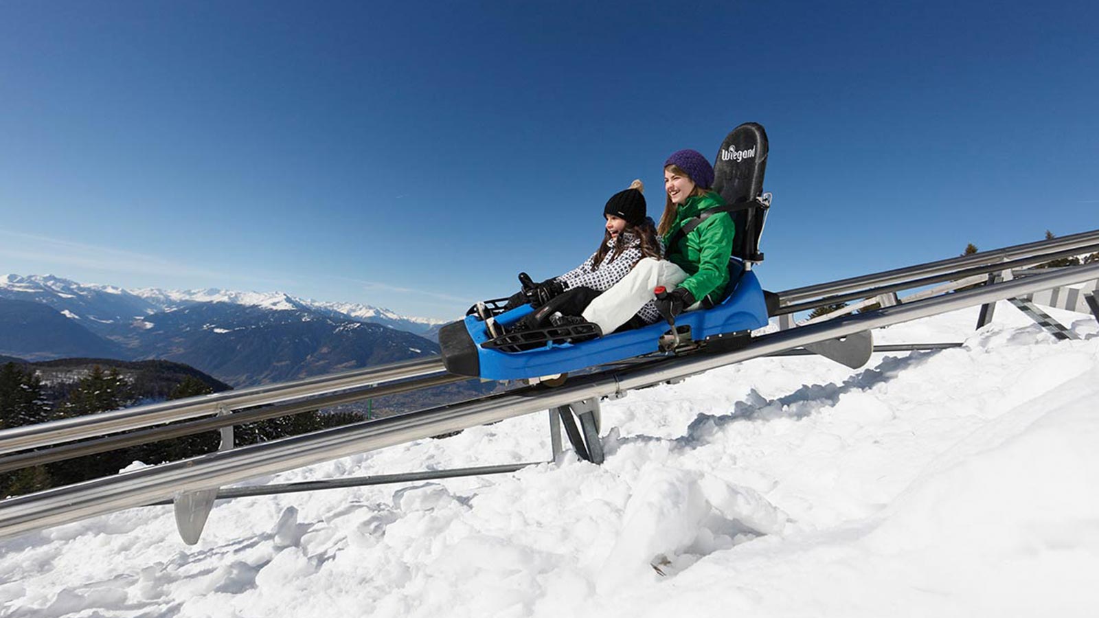 Zwei Mädchen auf dem Alpin-Bob-Schlitten auf Schienen