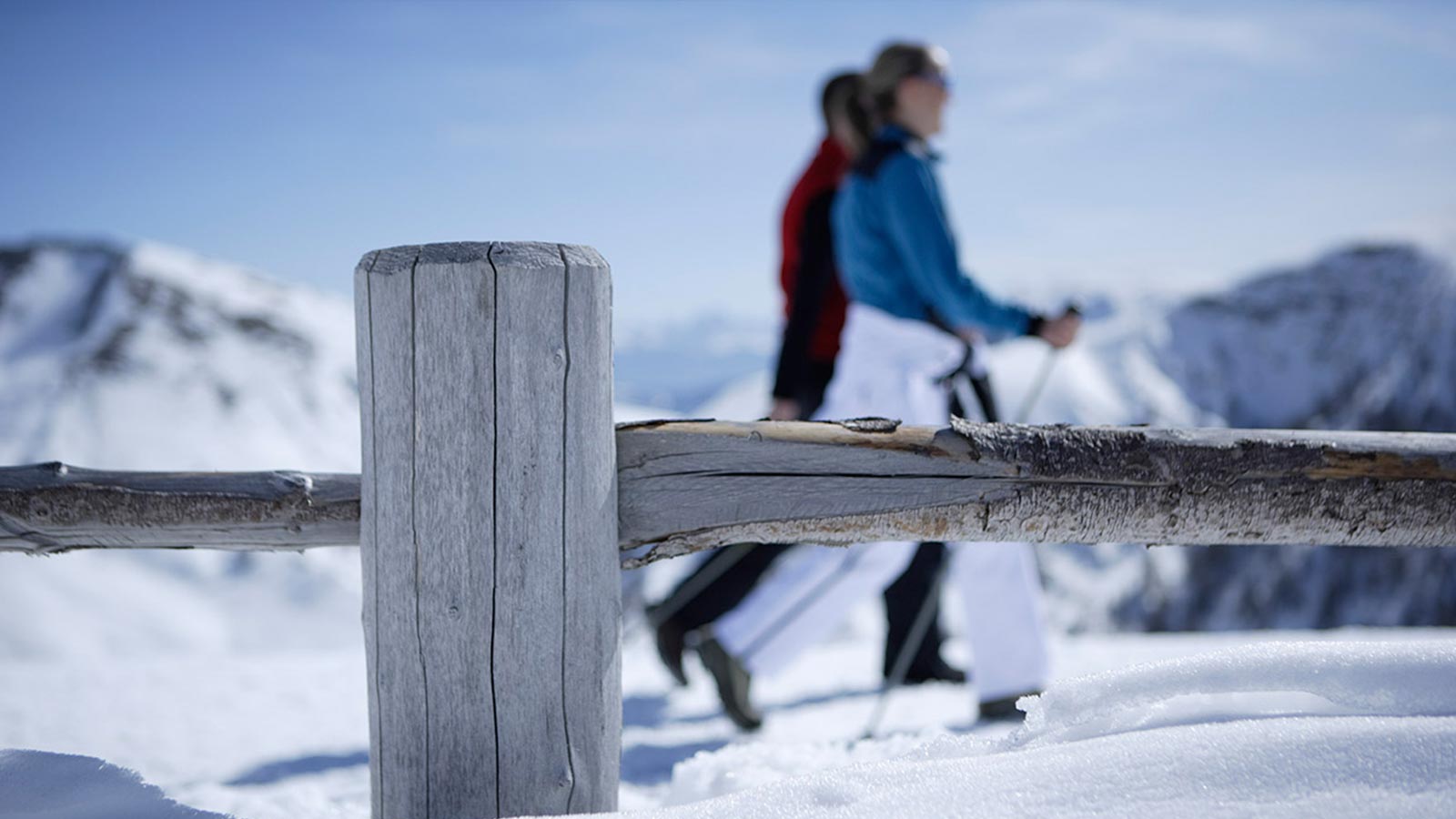 Detail eines Zauns mit einem im Schnee laufenden Paar im Hintergrund